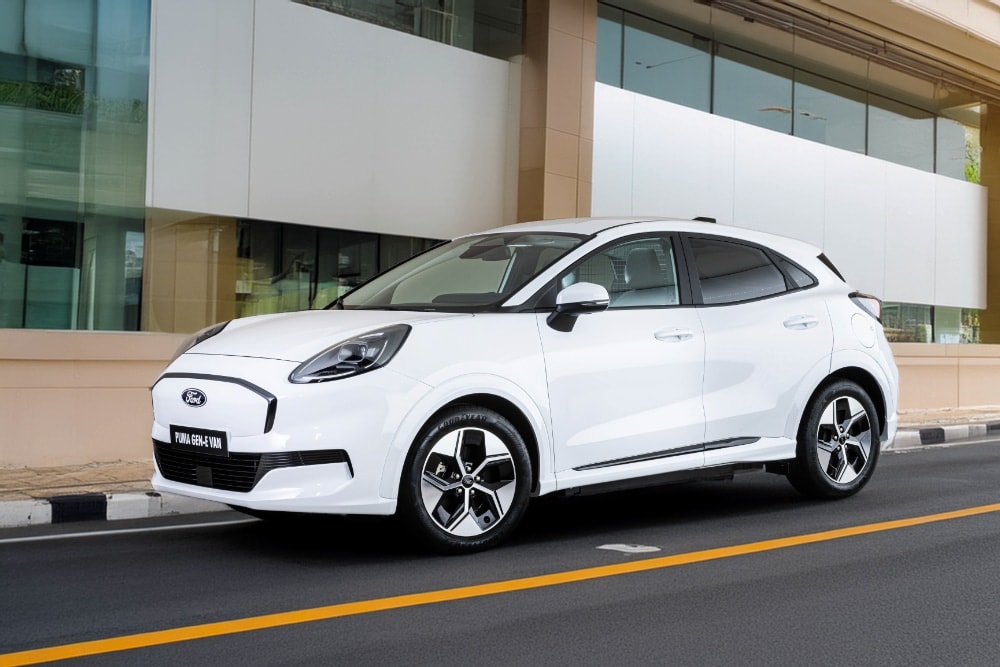 Λευκό Ford Puma Gen-E Van σταθμευμένο μπροστά από σύγχρονο κτίριο με γυάλινες επιφάνειες.