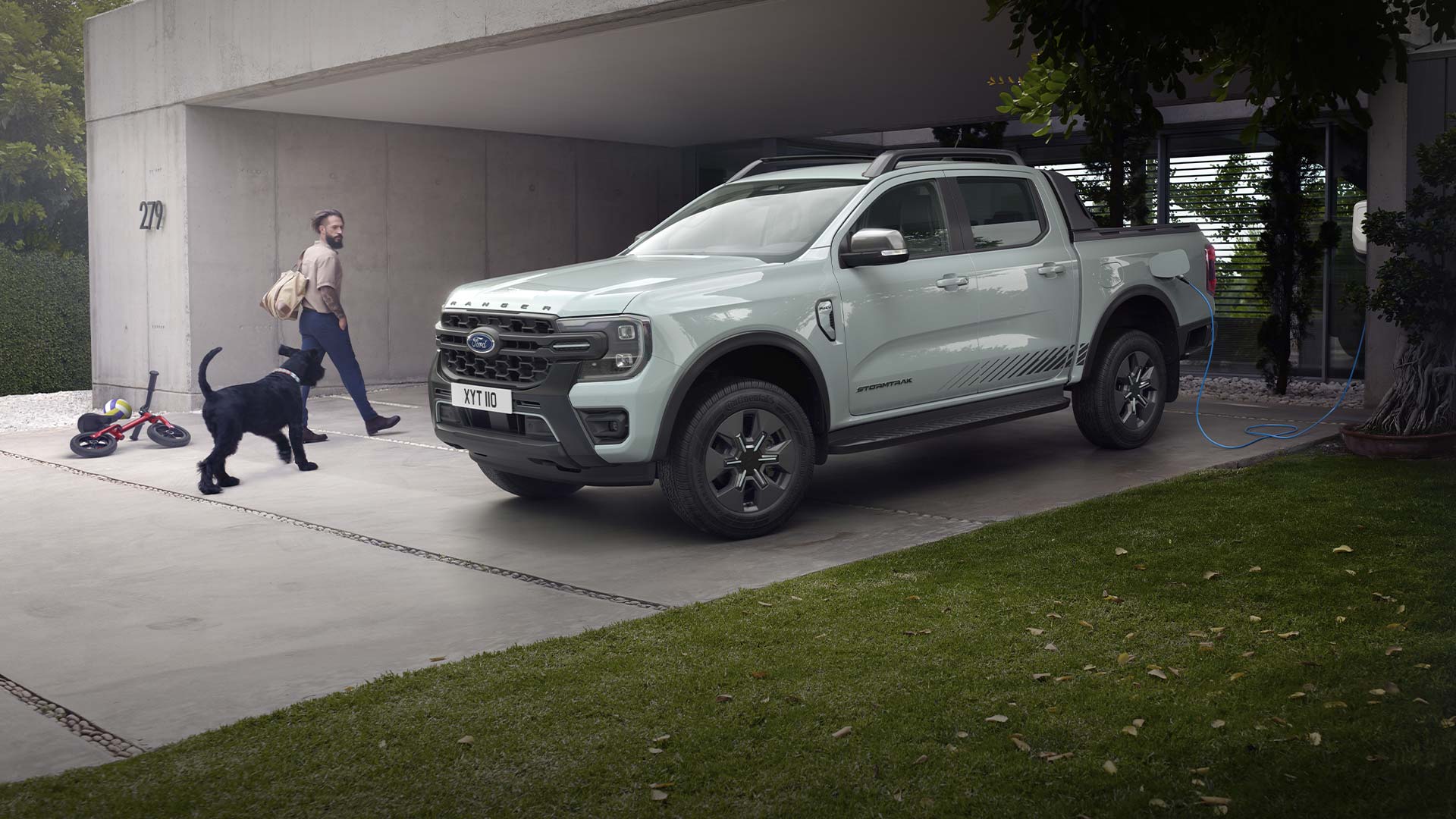 Ένα σταθμευμένο Ford Ranger Plug-In Hybrid συνδεδεμένο στη φόρτιση και δίπλα ένα άνδρας με έναν σκύλο περπατούν.