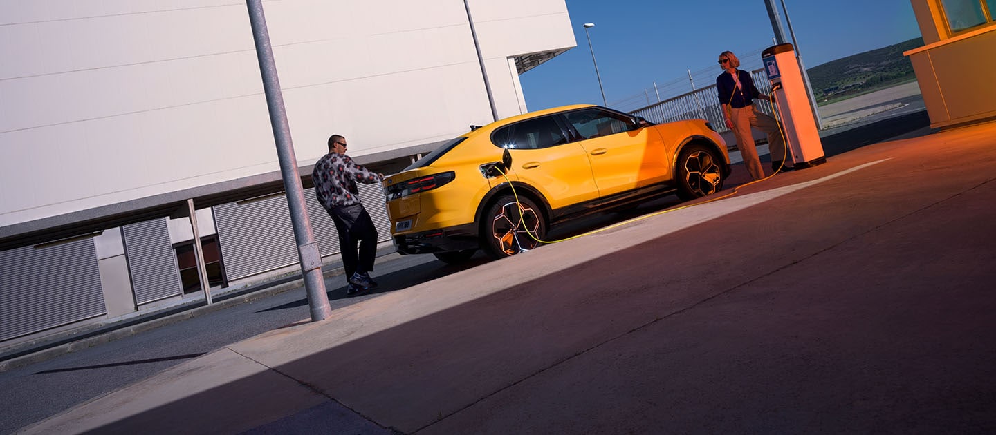 Άτομα φορτίζουν ένα κίτρινο Ford Capri EV σε δημόσιο σταθμό φόρτισης. 