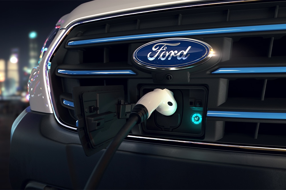 Κοντινή λήψη της θύρας φόρτισης του Ford E-Transit και του μπλε οβάλ λογότυπου Ford στη μάσκα.