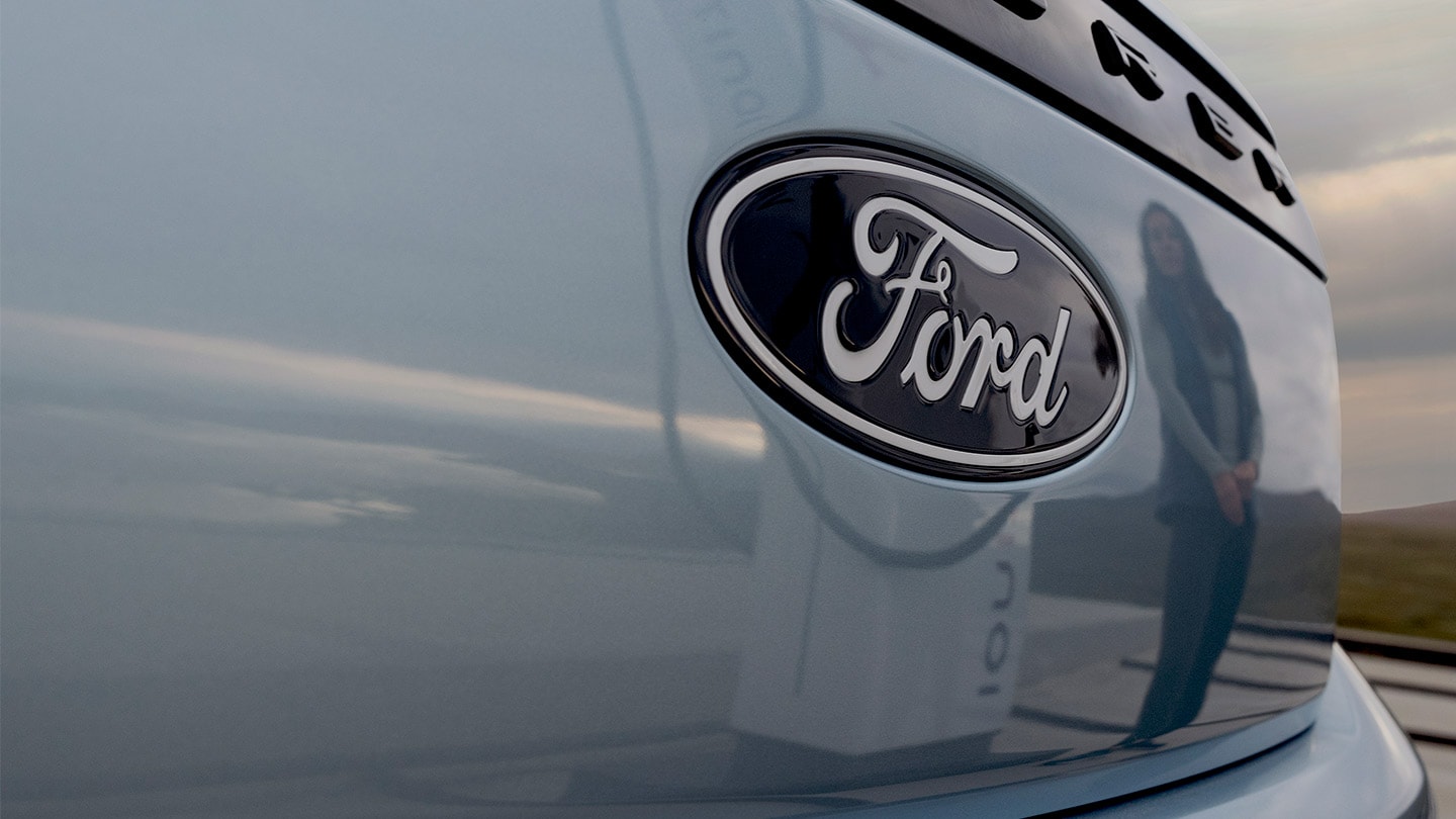 Λογότυπο Ford σε ένα μπλε ηλεκτρικό Ford Explorer με το δημόσιο σταθμό φόρτισης αντανακλώμενο στο αυτοκίνητο.