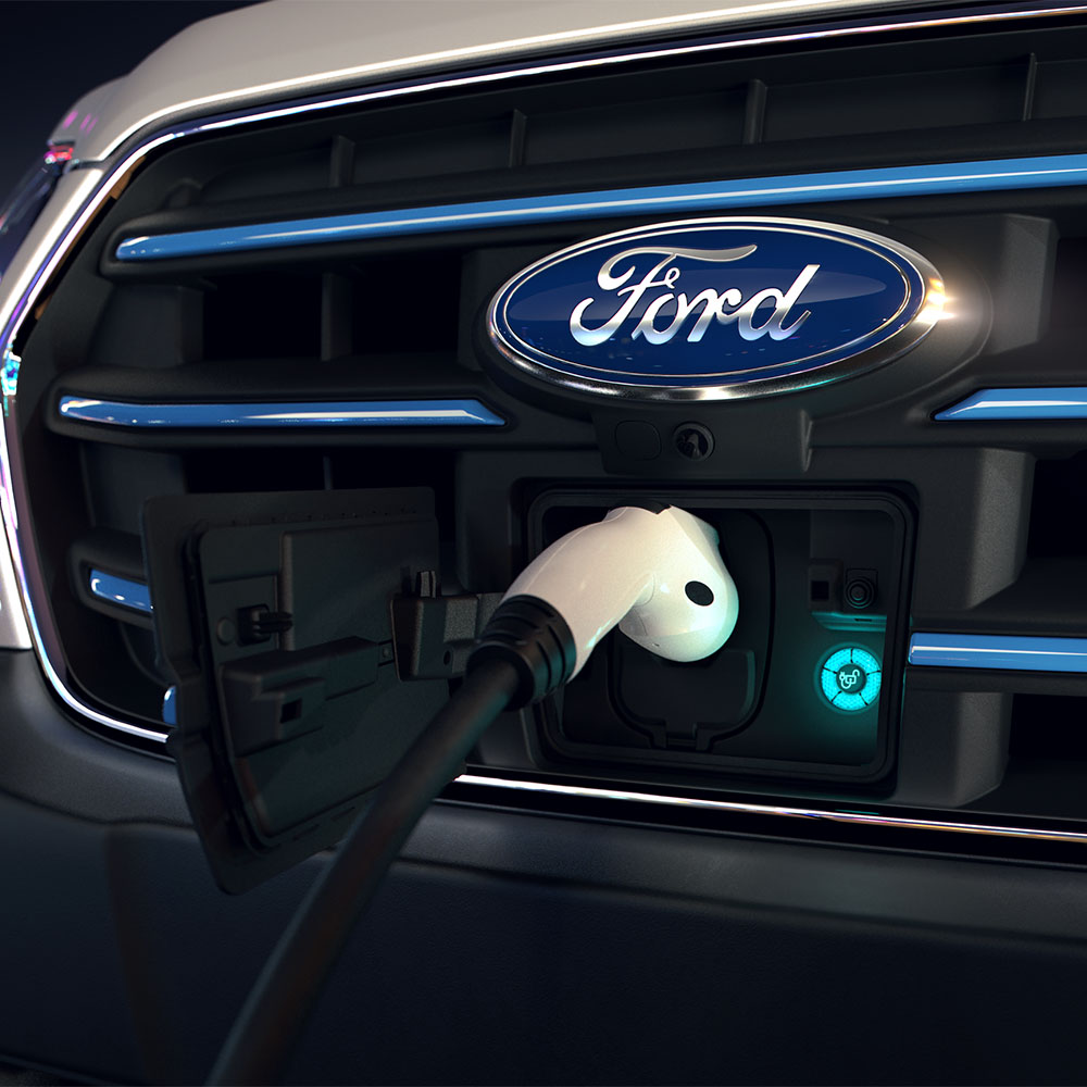 Κοντινό πλάνο ενός Ford E-Transit van σε σημείο φόρτισης και του μπλε οβάλ σήματος Ford στην μπροστινή μάσκα. 