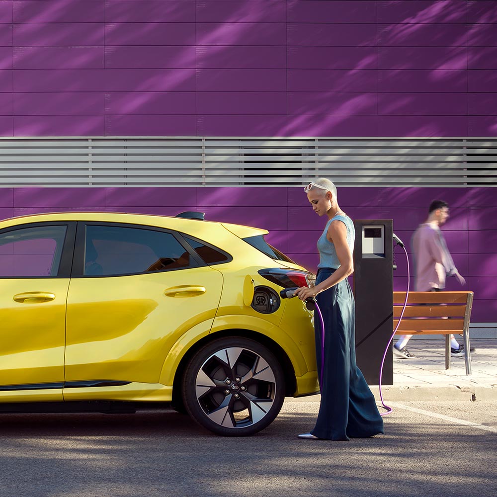 Ένας οδηγός συνδέει ένα ασημί Ford Mustang Mach-E σε δημόσιο σταθμό φόρτισης για εύκολη φόρτιση EV.
