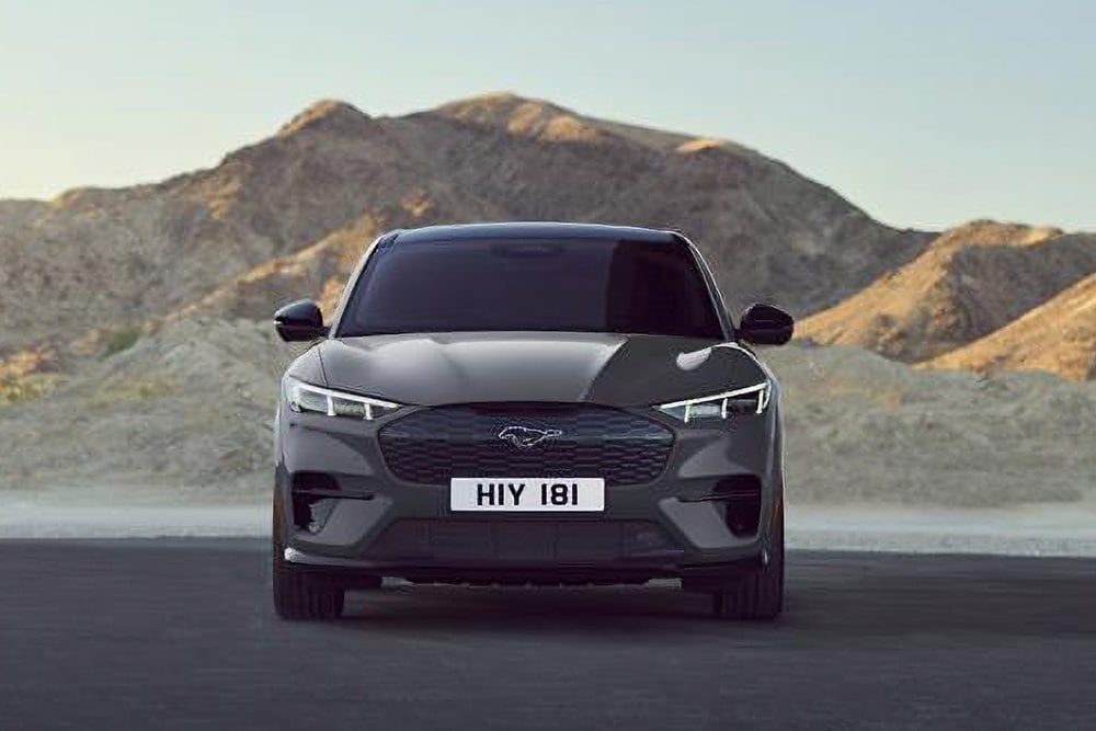 Μπροστινή όψη μιας μαύρης Ford Mustang Mach-E, που βρίσκεται σταθμευμένη μπροστά σε ένα ορεινό τοπίο.