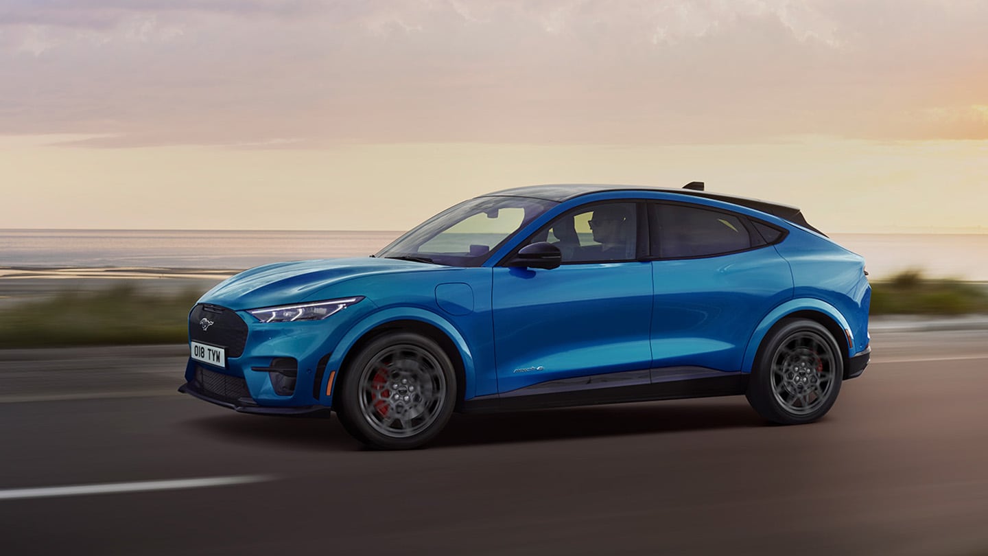 Πλάγια εμφάνιση της Ford Mustang Mach-E που κινείται κατά μήκος ενός παραλιακού δρόμου.