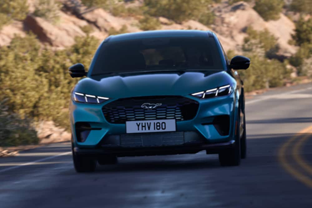 Μπροστινή άποψη μιας μπλε Ford Mustang Mach-E που κινείται σε ορεινό δρόμο.