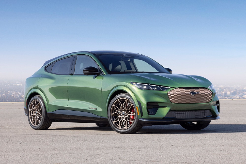 Πράσινη Ford Mustang Mach-E σταθμευμένη μπροστά σε ορίζοντα πόλης.