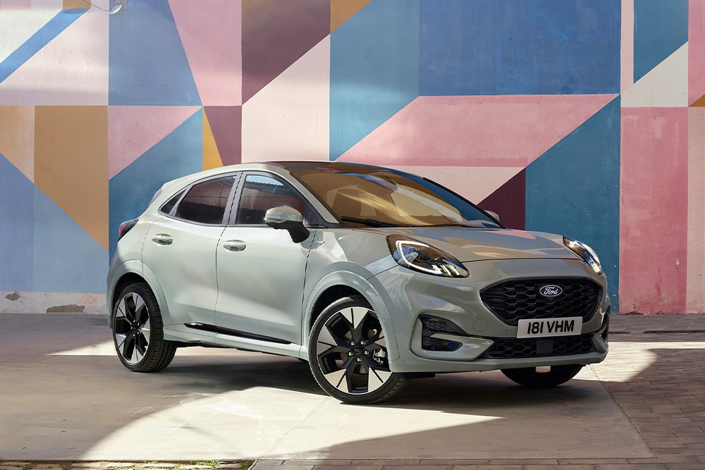 Ασημί Ford Puma SUV σταθμευμένο μπροστά από πολύχρωμο γεωμετρικό τοιχίο.