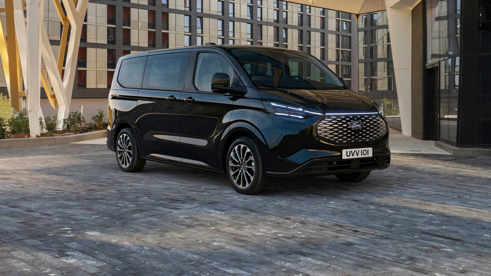 Μαύρο Ford E-Tourneo Custom σταθμευμένο μπροστά από ένα μοντέρνο κτήριο.