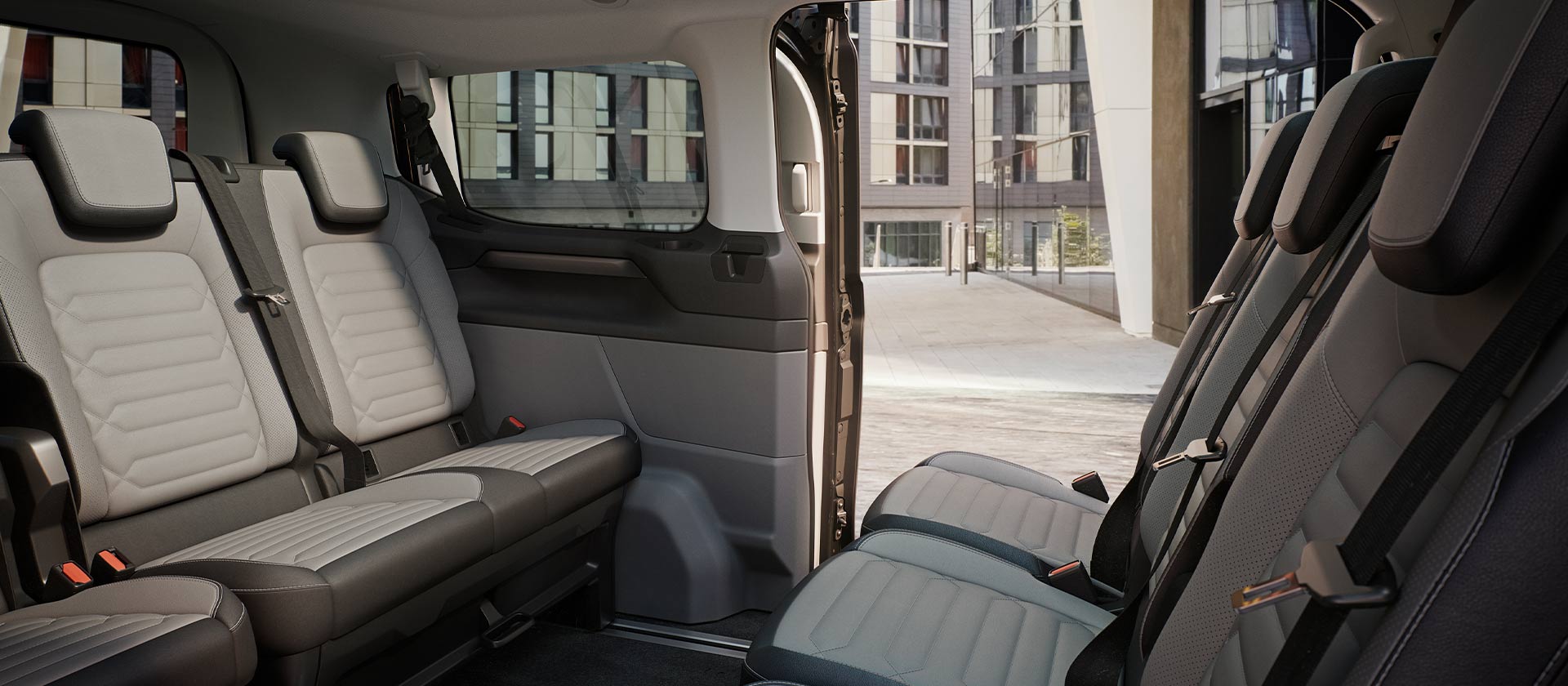 Εσωτερική άποψη του Ford Tourneo Custom, όπου φαίνονται πολλές σειρές γκρι καθισμάτων για τους επιβάτες, καθώς και η πανοραμική ηλιοροφή.