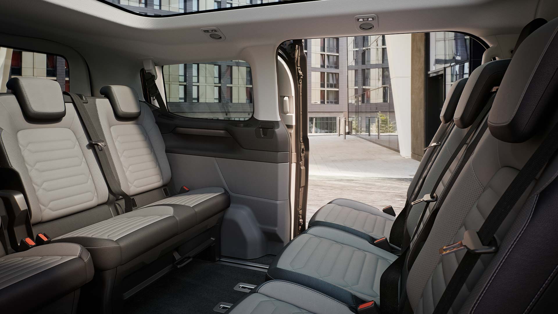 Εσωτερική άποψη του Ford Tourneo Custom, όπου φαίνονται πολλές σειρές γκρι καθισμάτων για τους επιβάτες, καθώς και η πανοραμική ηλιοροφή.