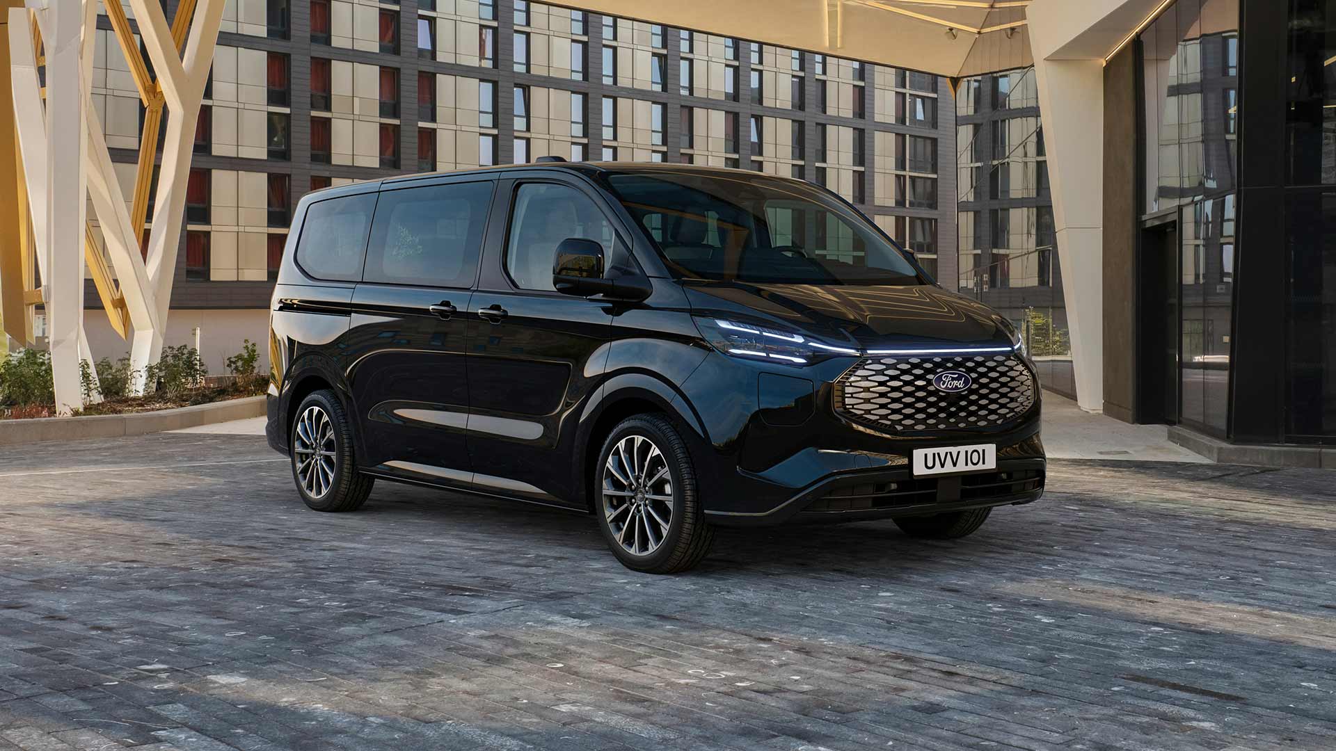 Μαύρο Ford E-Tourneo Custom σταθμευμένο μπροστά από ένα μοντέρνο κτήριο.