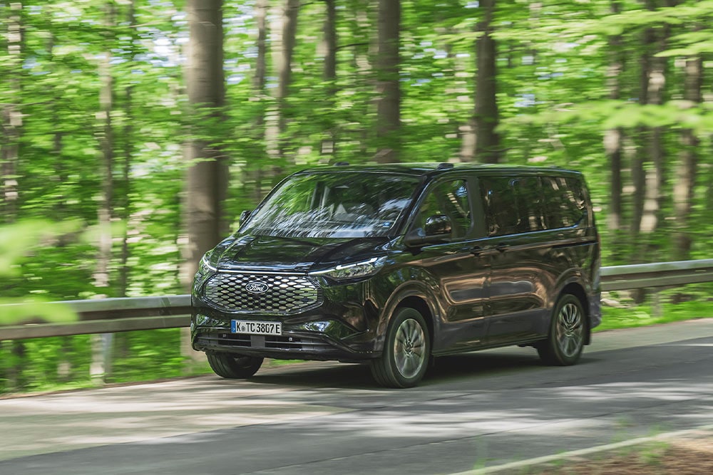 Μαύρο Ford E-Tourneo Custom που κινείται σε δεντρόφυτο δρόμο.