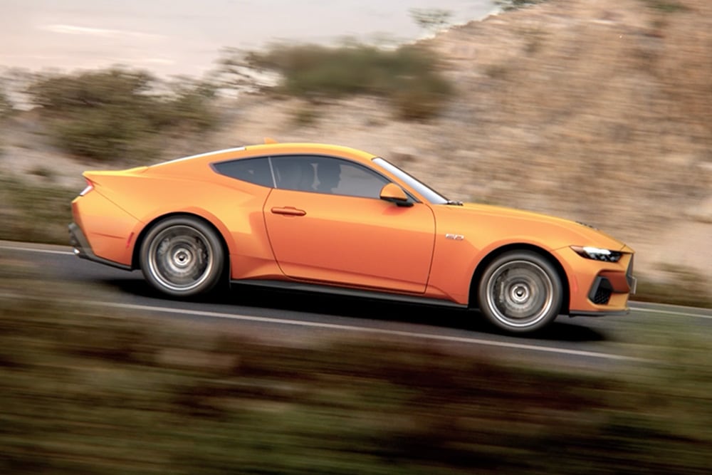 Πλάγια όψη της Ford Mustang GT Fastback σε χρώμα Orange Fury, που κινείται σε έναν δρόμο
