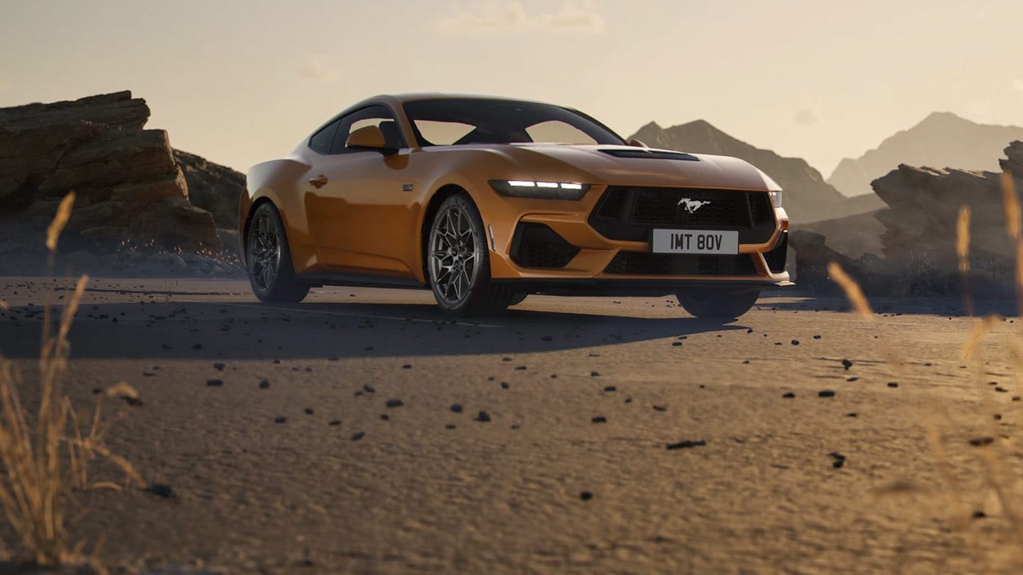 Πλευρική όψη μιας πορτοκαλί Ford Mustang, παρκαρισμένης σε ένα βραχώδες, ερημικό τοπίο.