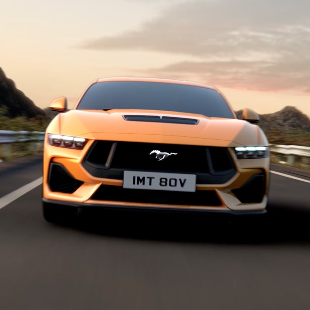 Μπροστινή όψη μιας πορτοκαλί Ford Mustang με κοντινό πλάνο στους προβολείς, τη μάσκα και το σήμα Mustang
