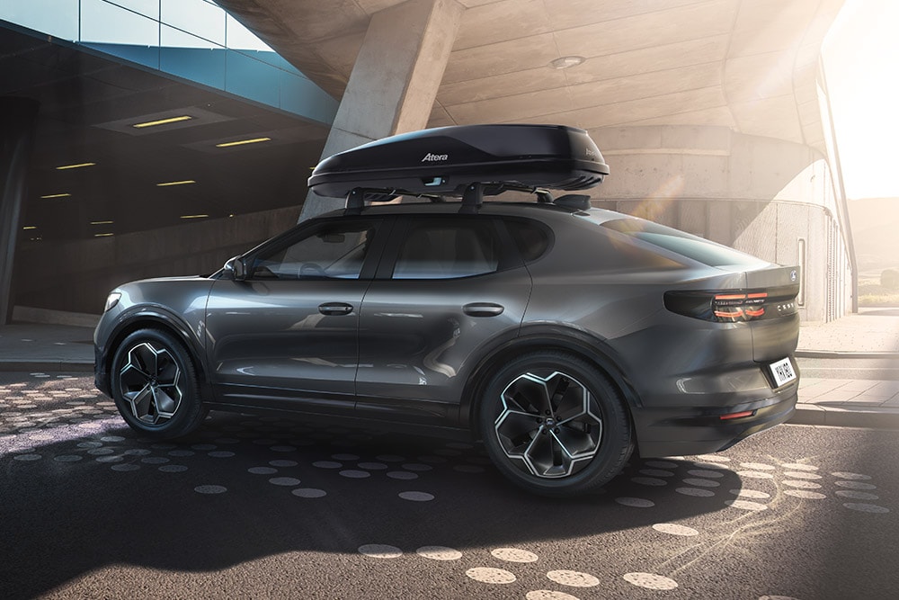 Πλάγια 3/4 όψη ενός κόκκινου Ford Capri με μπαγκαζιέρα οροφής, παρκαρισμένο κάτω από μια μοντέρνα κτιριακή δομή.