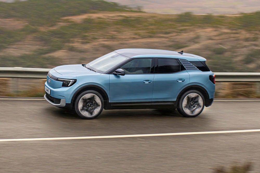 Πλάγια όψη ενός γαλάζιου Ford Explorer που οδηγεί σε βρεγμένο δρόμο με θολό φόντο