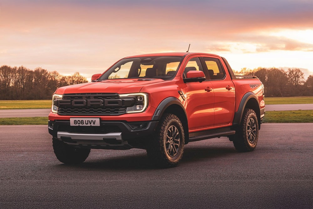 Ένα πορτοκαλί φορτηγάκι Ford Ranger Raptor σταθμευμένο σε ένα γραφικό τοπίο.