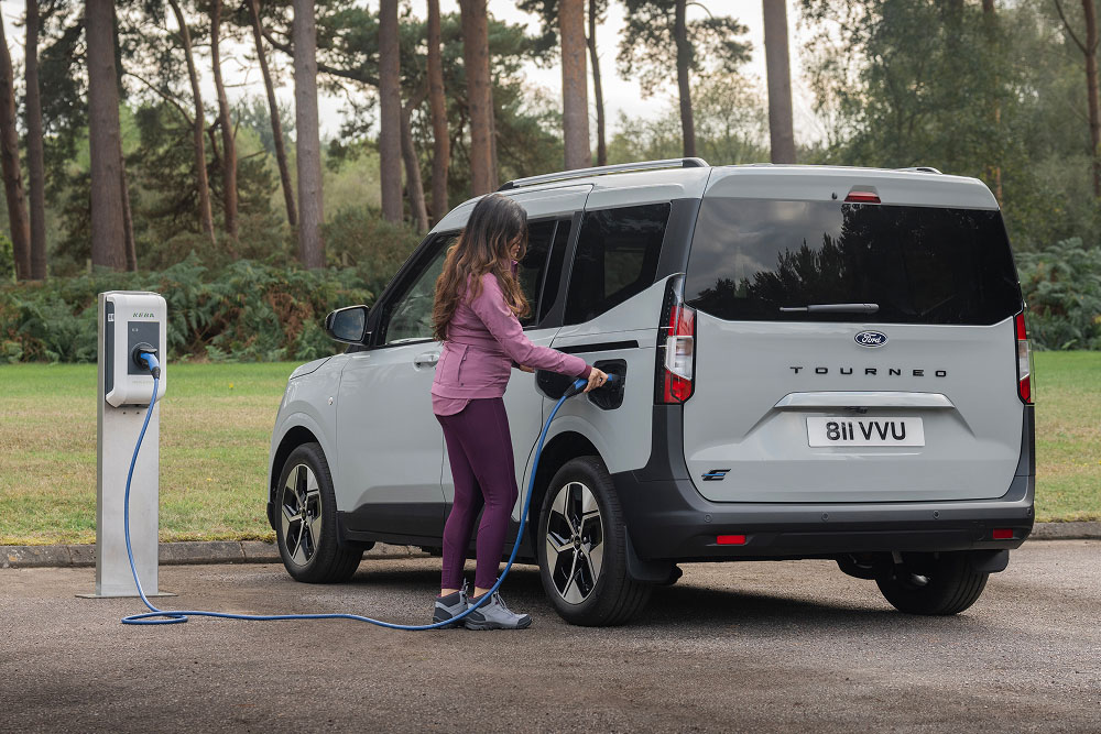 Ένα άτομο συνδέει ένα γκρι Ford E-Tourneo Courier σε έναν εξωτερικό σταθμό φόρτισης.