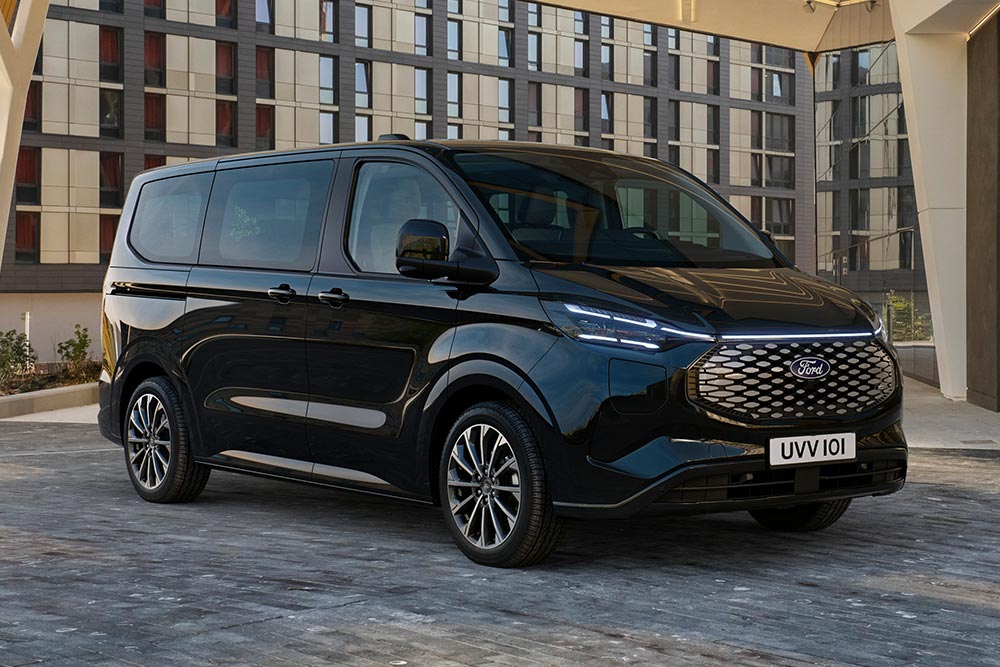 Μαύρο Ford E-Tourneo Custom σταθμευμένο μπροστά από ένα μοντέρνο κτήριο.