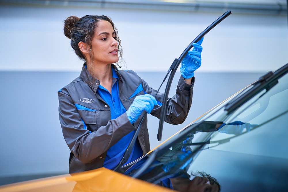 Τεχνικός της Ford με μπλε γάντια ρυθμίζει υαλοκαθαριστήρα σε όχημα.
