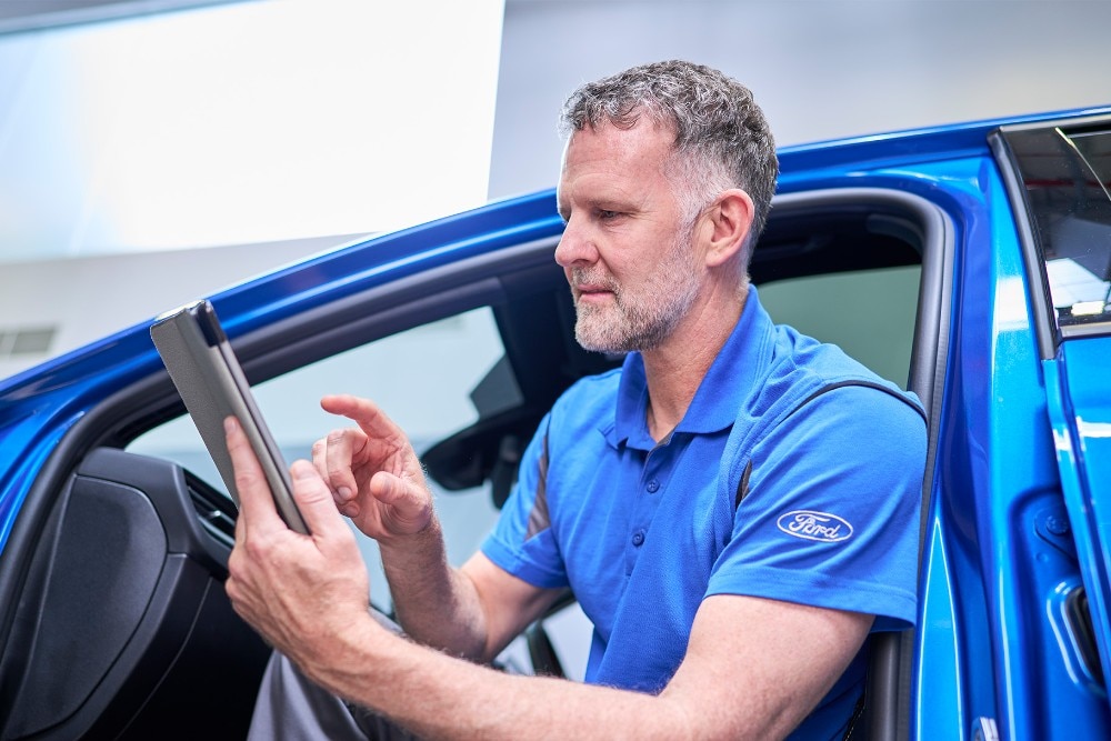 Τεχνικός Ford μέσα σε μπλε όχημα κρατάει φορητό υπολογιστή