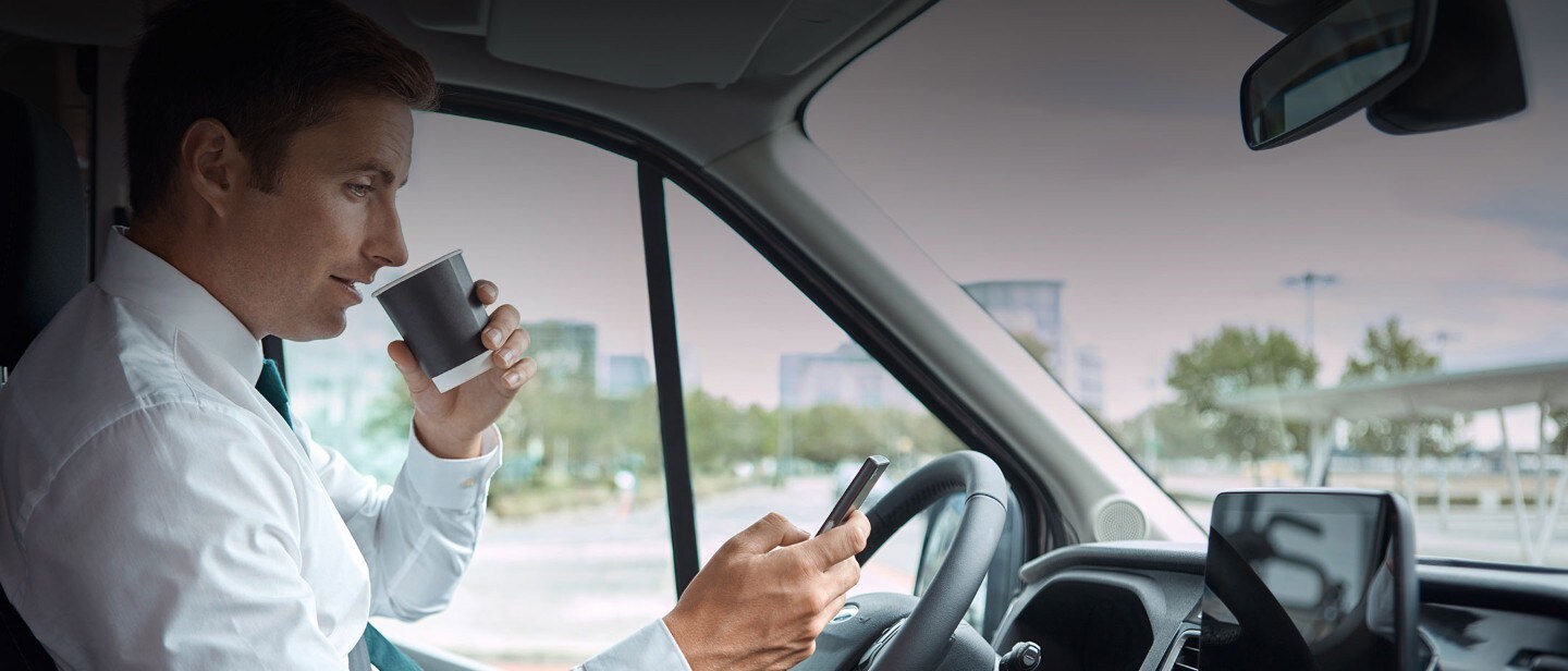 Man drinking coffee and checking mobile phone in car