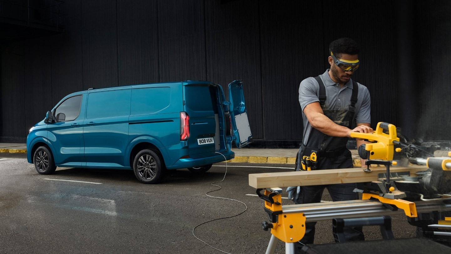 Man cutting wood in front of blue Transit Custom Plug-In Hybrid Van