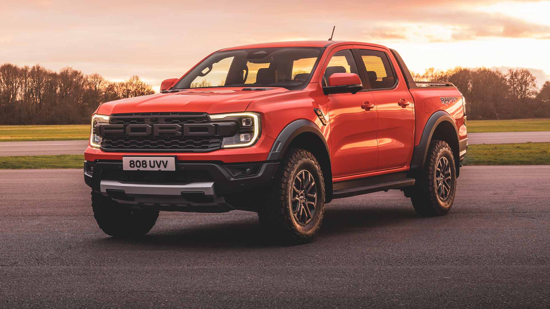 Ένα Ford Ranger Raptor σε Code Orange σταθμευμένο σε πίστα με τους προβολείς ανοιχτούς. 