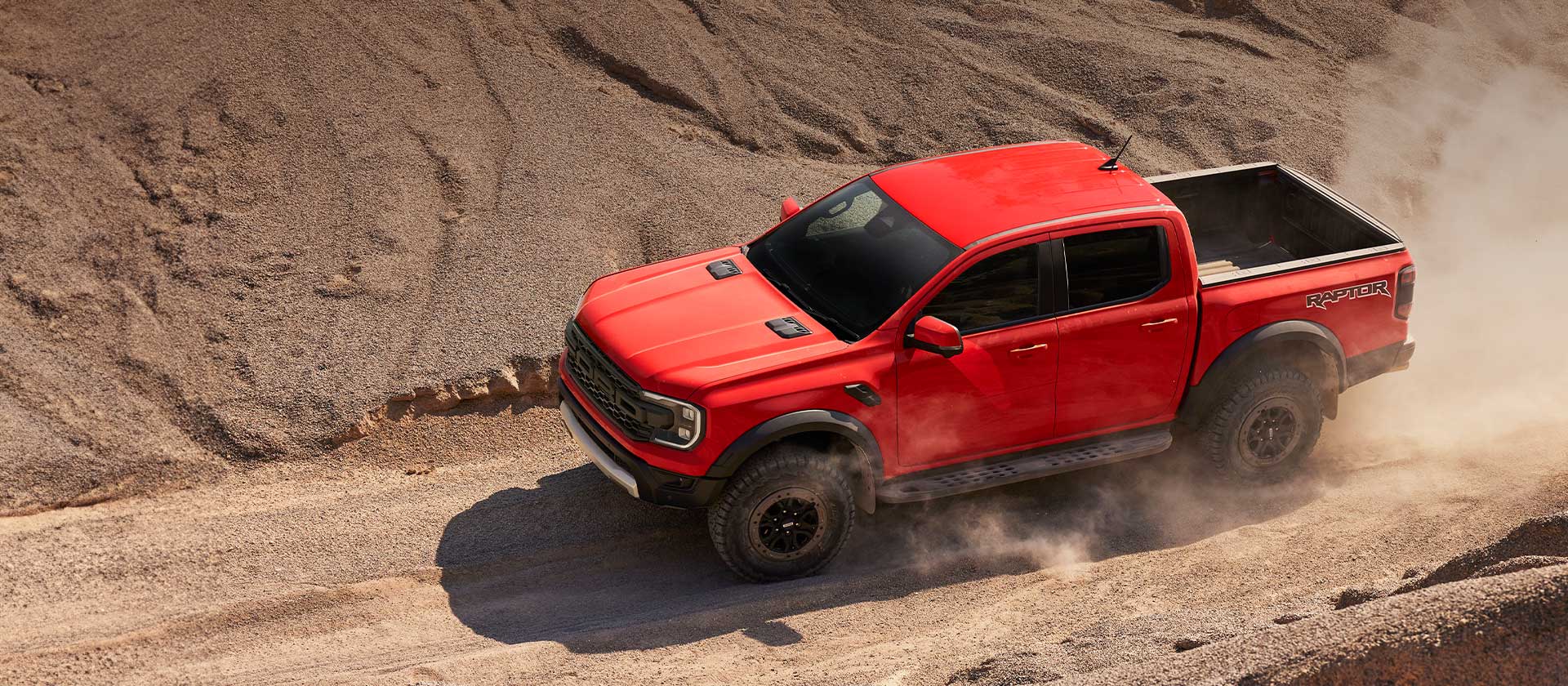 Ένα Ford Ranger Raptor σε Code Orange κινείται σε ανηφόρα μέσα από σκόνη.