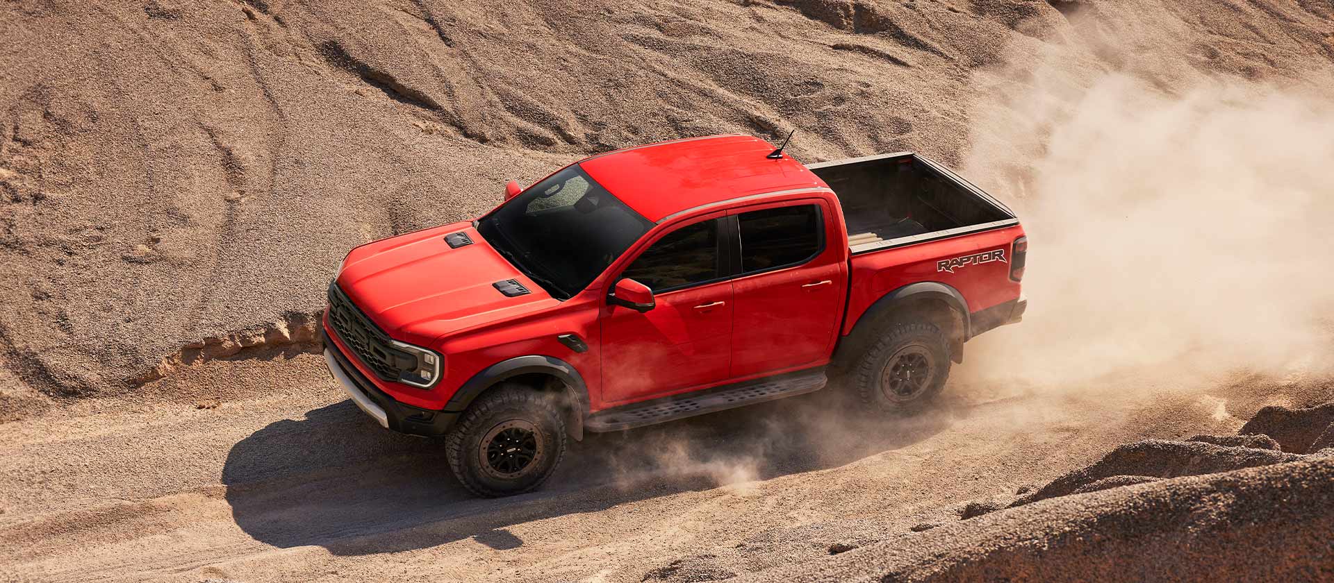 Ένα Ford Ranger Raptor σε Code Orange κινείται σε ανηφόρα μέσα από σκόνη.