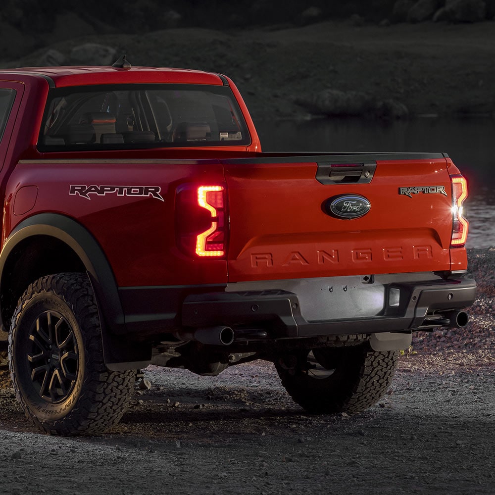 Πίσω όψη ενός Ford Ranger Raptor σε Code Orange με ανοιχτά τα πίσω φώτα.