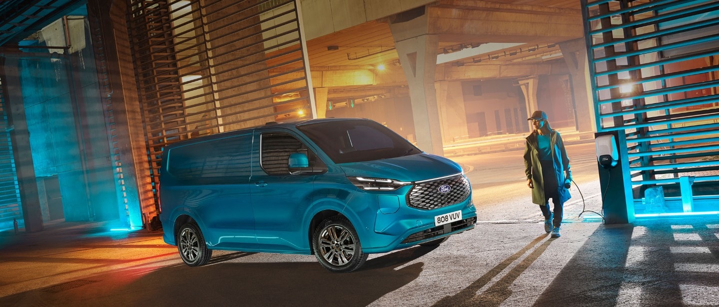 Blue Ford E-Transit Custom parked up with a person walking beside Blue Ford E-Transit Custom parked up with a person walking beside