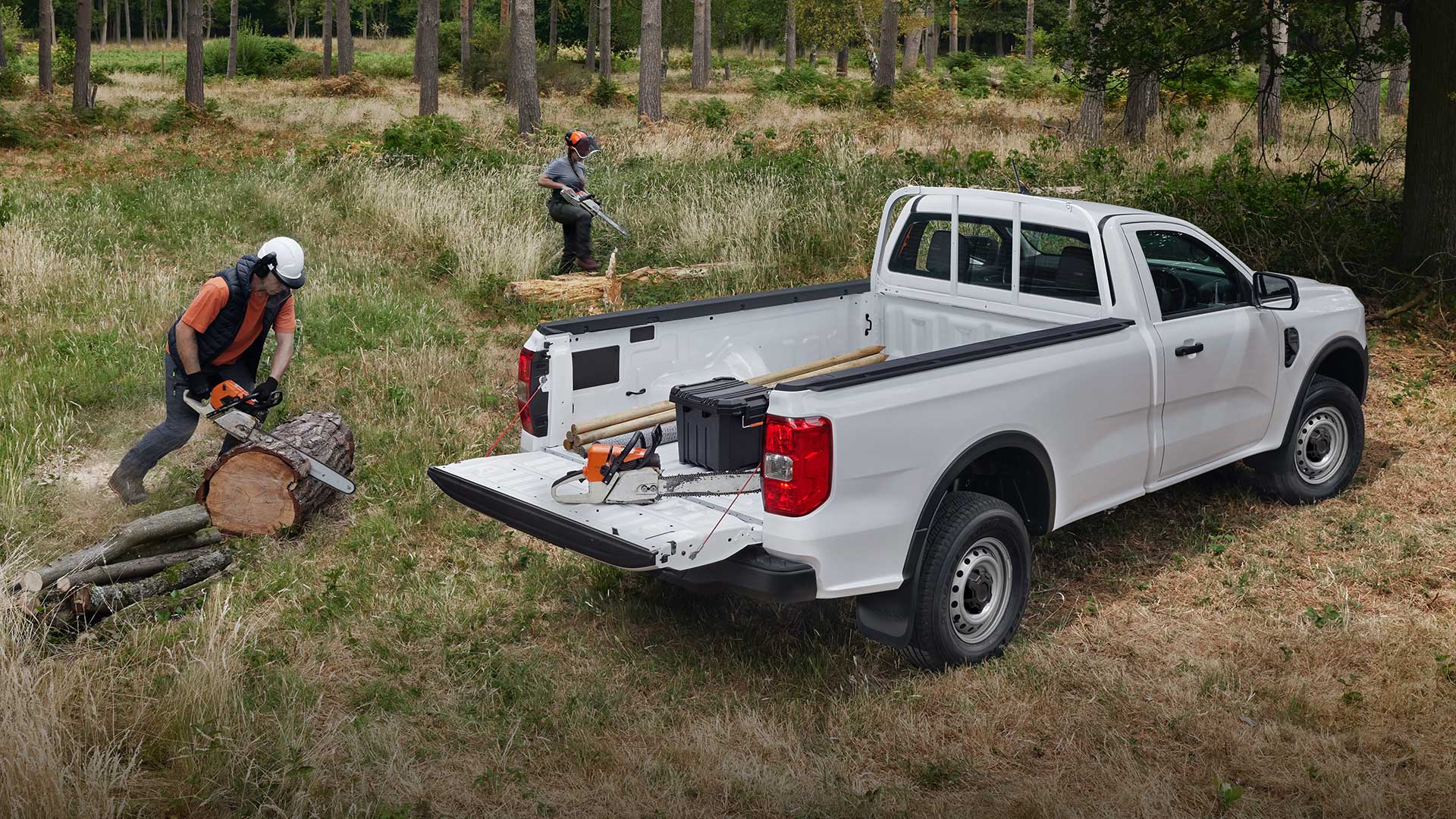 Λευκό Ford Ranger Single Cab σταθμευμένο σε γρασίδι με την πίσω πόρτα ανοιχτή. Ένα άτομο κοντά κόβει κορμούς με αλυσοπρίονο.