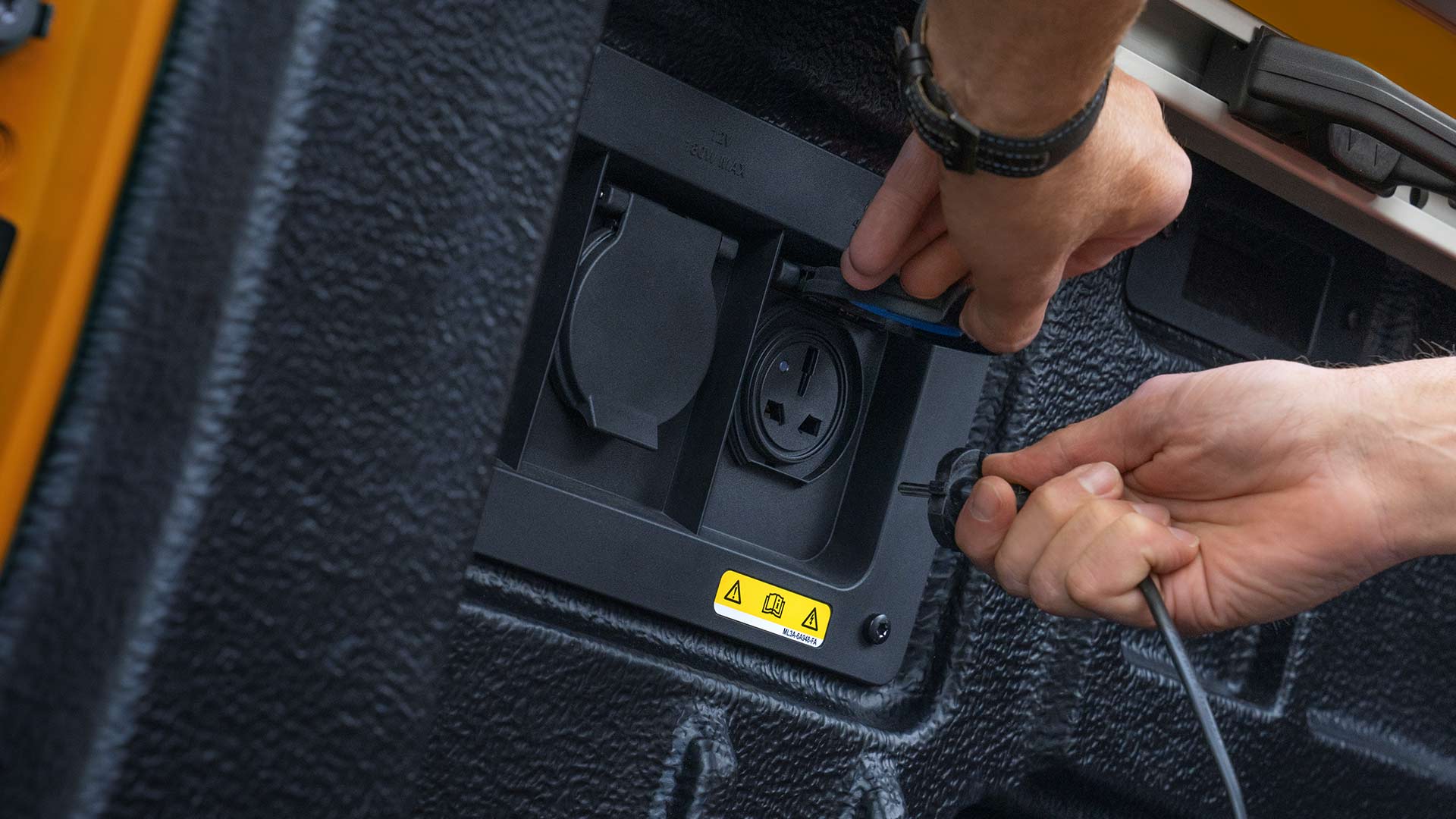 Κοντινό πλάνο σε χέρια που συνδέουν τα καλώδια στην πρίζα στον χώρο φόρτωσης του Ford Ranger.