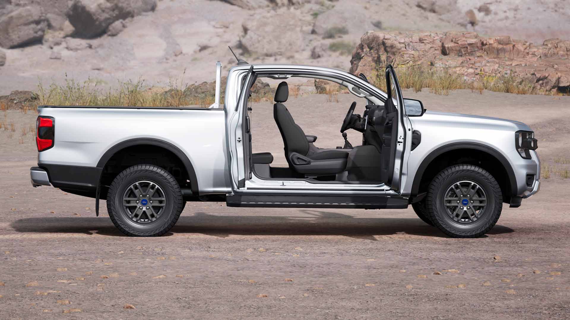 Προφίλ ενός ασημί Ford Ranger Rap Cab XLT με ανοιχτές πόρτες, σταθμευμένο σε σκονισμένο έδαφος.