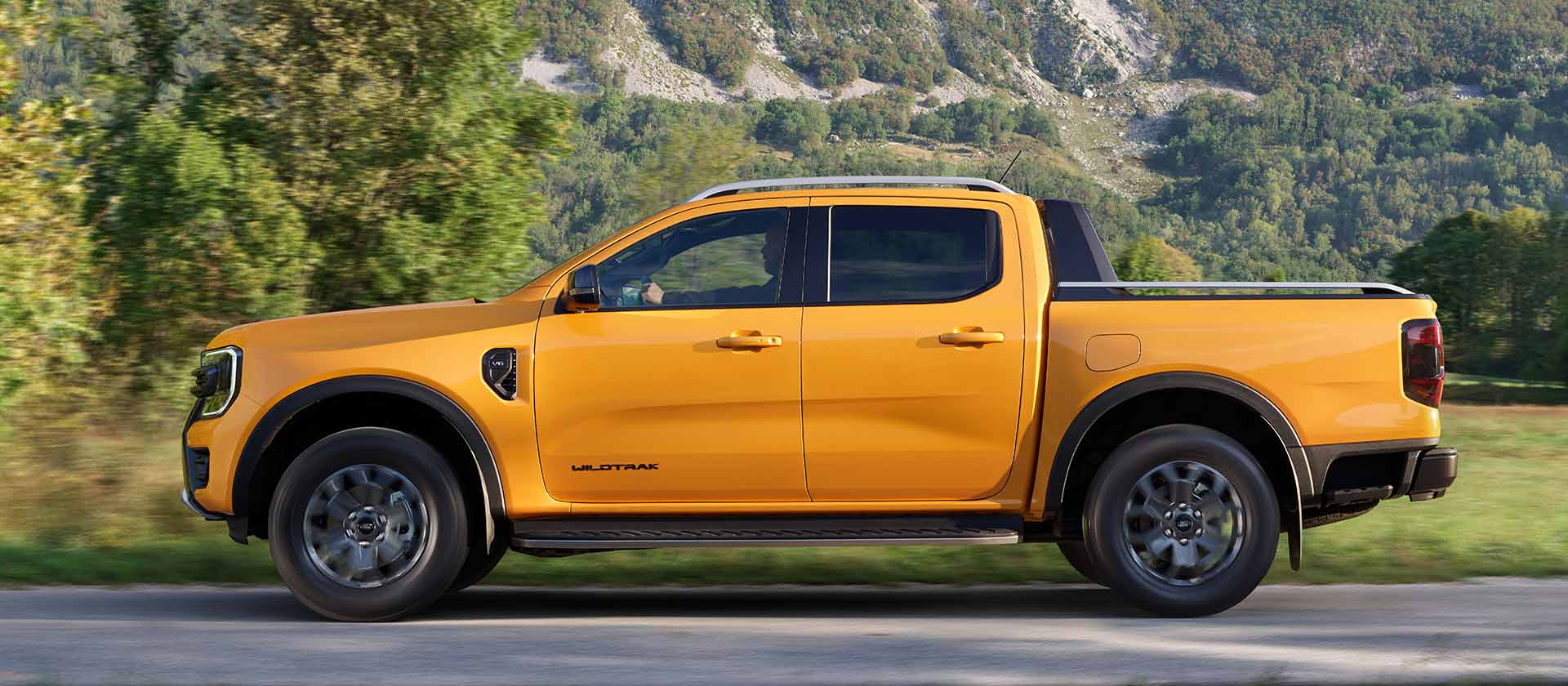 Πλευρικό προφίλ ενός κίτρινου Ford Ranger Double Cab Wildtrak σταθμευμένο στην άκρη του δρόμου σε ορεινό τοπίο.