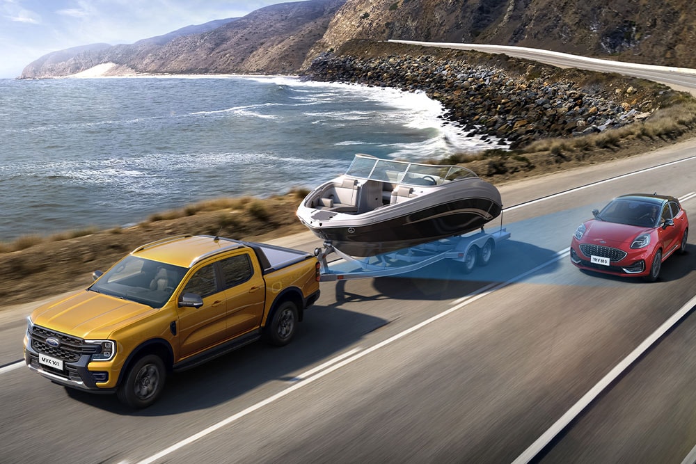 Ένα κίτρινο Ford Ranger ρυμουλκεί μια βάρκα κατά μήκος ενός παράκτιου αυτοκινητόδρομου, επιδεικνύοντας την ικανότητα ρυμούλκησης.
