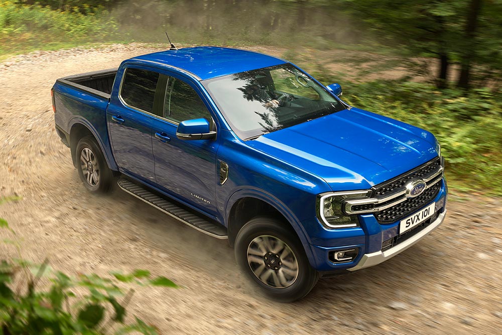 Ένα μπλε φορτηγό Ford Ranger κινείται κατά μήκος ενός χωματόδρομου μέσα σε ένα δάσος, αφήνοντας ίχνη σκόνης.