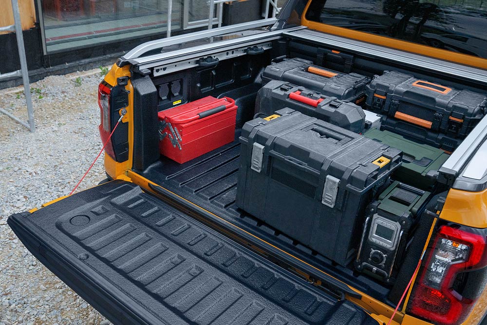 Η πίσω πόρτα ενός κίτρινου Ford Ranger είναι ανοιχτή, με μια ξύλινη σανίδα ασφαλισμένη πάνω της με σφιγκτήρα.