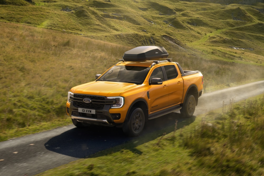Κίτρινο Ford Ranger οδηγείται σε αγροτικό δρόμο με ένα κουτί οροφής τοποθετημένο στις μπάρες οροφής.