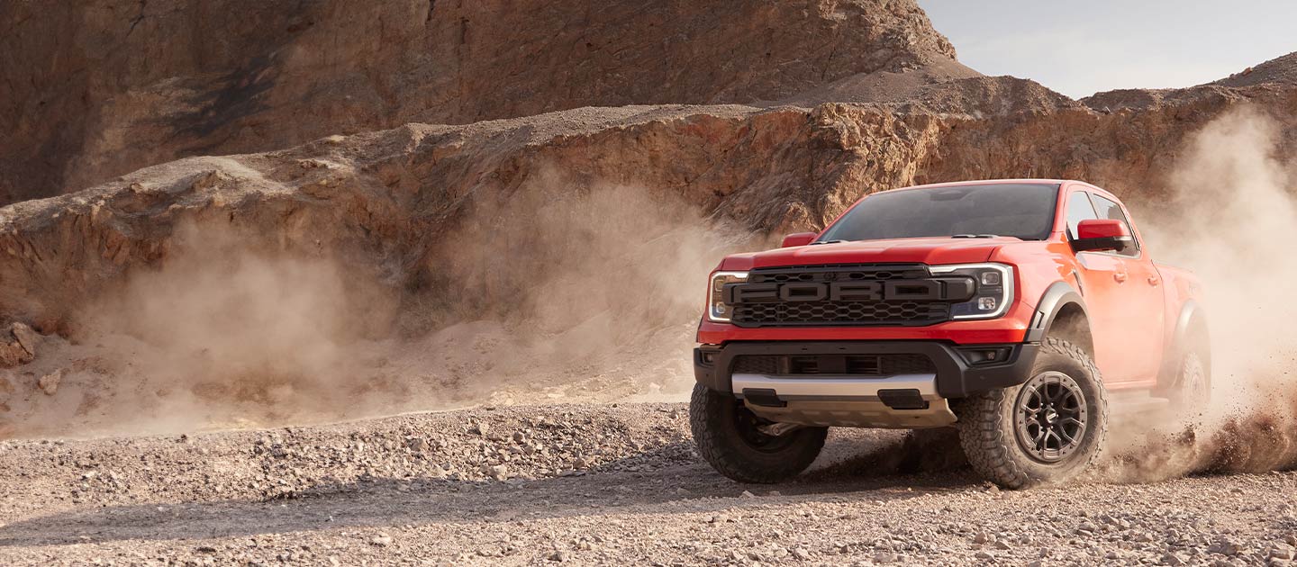 Ένα κόκκινο Ford Ranger Raptor σηκώνει σκόνη καθώς κινείται σε ένα τοπίο ερήμου.
