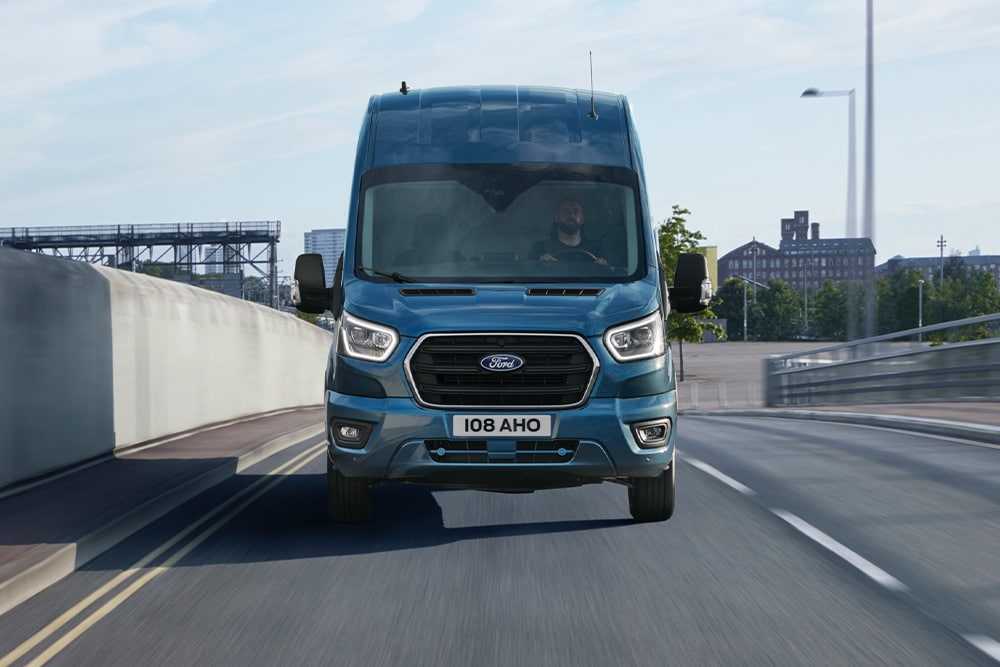 Μπροστινή άποψη ενός μπλε Ford Transit Van που κινείται σε έναν δρόμο.