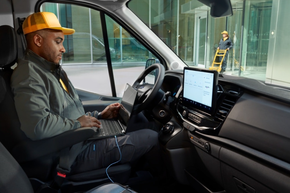 Άνδρας που κάθεται στη θέση του οδηγού ενός Ford Transit van και χρησιμοποιεί φορητό υπολογιστή.
