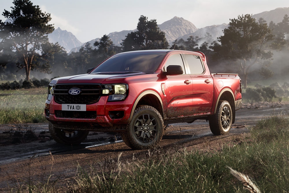 Κόκκινο Ford Ranger Raptor που κινείται σε χωματόδρομο μέσα από ένα γραφικό τοπίο.