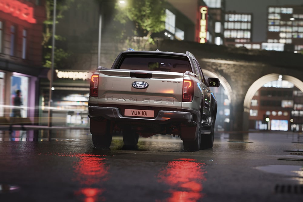 Πίσω όψη ενός ασημένιου Ford Ranger που διασχίζει ένα αστικό τοπίο με νέον φωτισμό τη νύχτα.