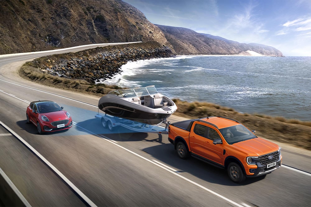 Πορτοκαλί Ford Ranger που ρυμουλκεί μια βάρκα κατά μήκος ενός παράκτιου αυτοκινητόδρομου, επιδεικνύοντας την ικανότητα ρυμούλκησης.