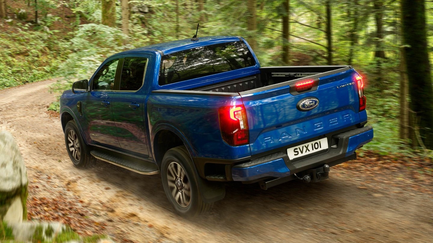 All-New Ranger in blue driving down forest road rear 3/4 view