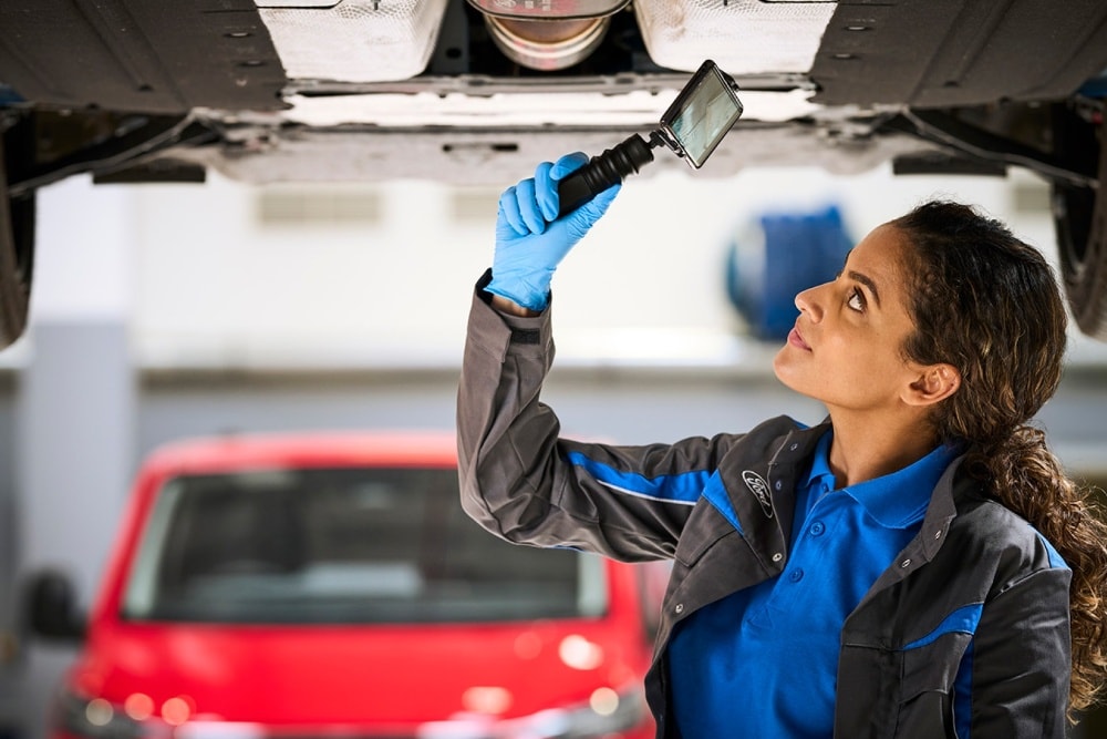 Ένας τεχνικός της Ford επιθεωρεί το κάτω μέρος ενός ανυψωμένου αυτοκινήτου με ψηφιακή κάμερα επιθεώρησης.